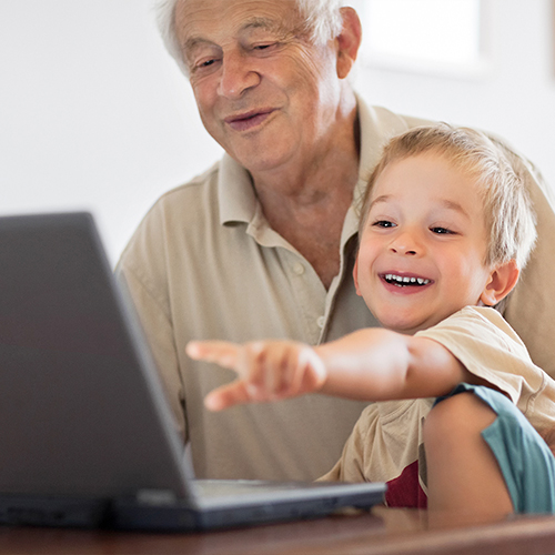 Grandfather And Little Grandson Looking At Laptop, Laughing Together